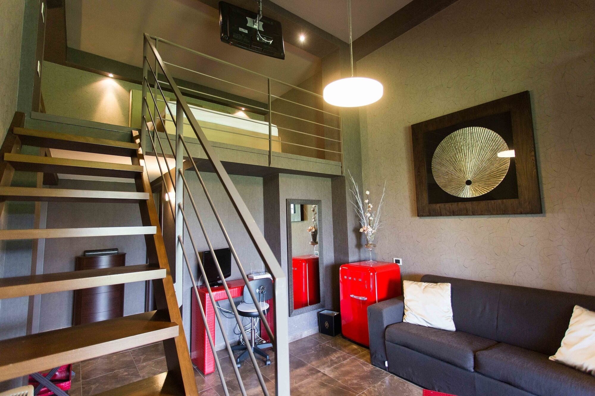 A modern living room with a staircase, a red refrigerator, a black sofa, and a wall-mounted decorative piece.