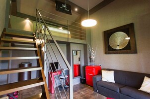 Una sala moderna con escalera, un refrigerador rojo, un sofá negro y un adorno en la pared.