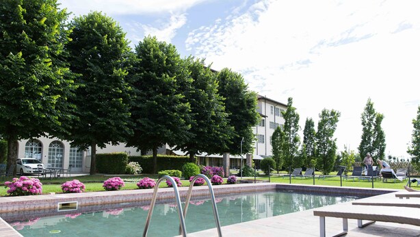 A swimming pool with a metal ladder, surrounded by a well-maintained lawn and trees. - Somaschi Hotel (Cherasco)