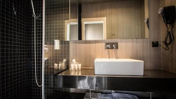 Un baño moderno con ducha de vidrio, lavamanos blanco y secador de pelo montado en la pared.
