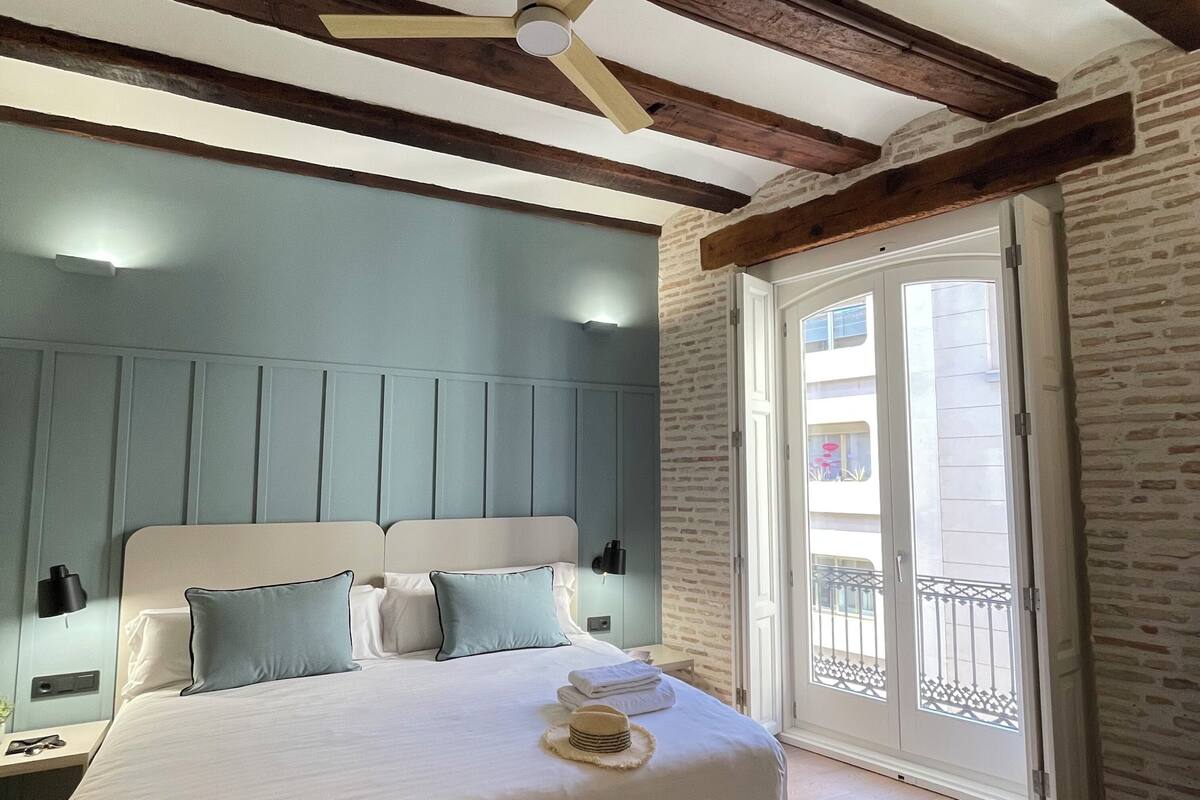 A bedroom with a bed, a nightstand, a ceiling fan, and a door leading to a balcony.