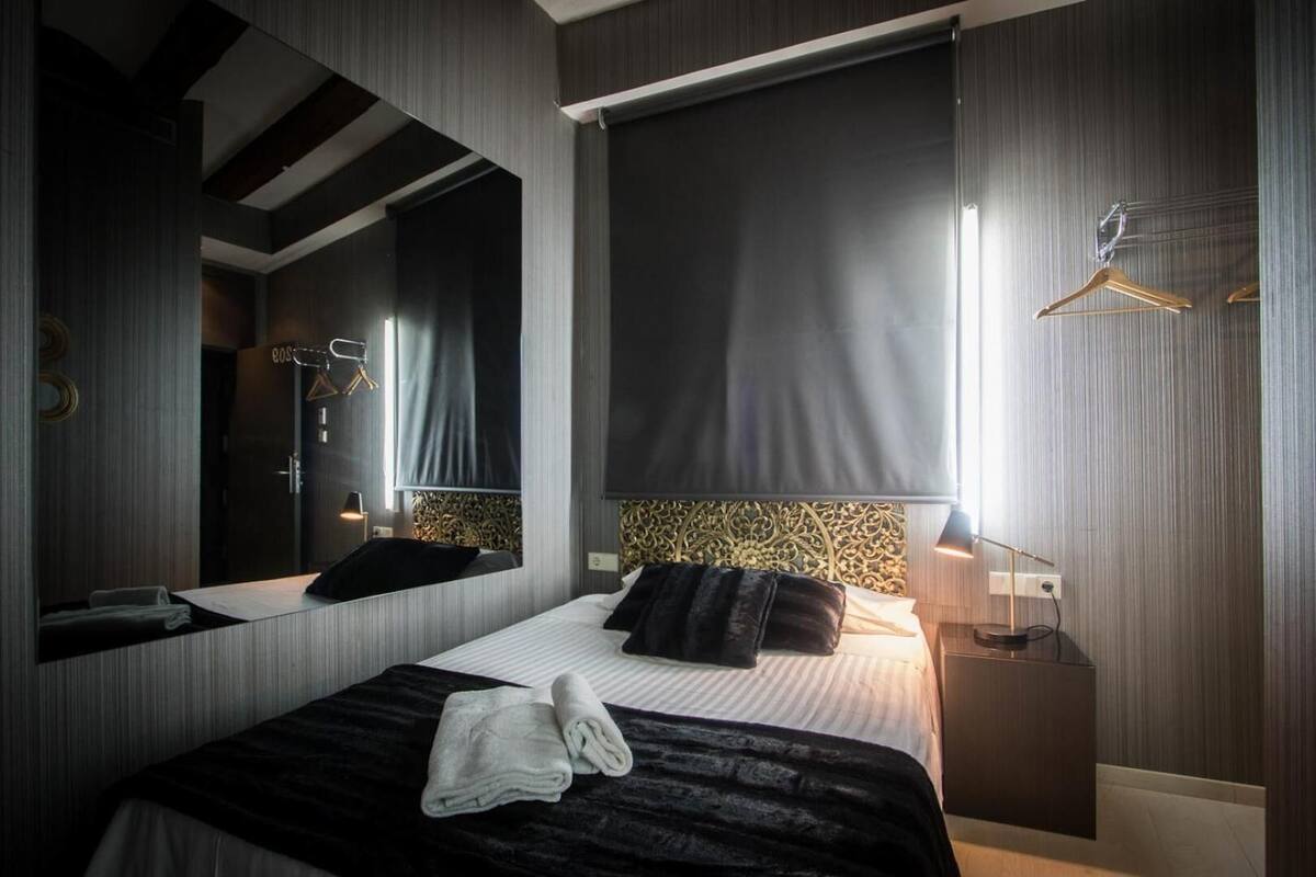 A modern hotel room with a large bed, a mirror, a bedside table, and a wardrobe.