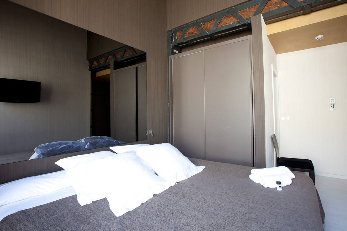 A hotel room with a large bed, a flat-screen TV mounted on the wall, a wardrobe, and a mirror.
