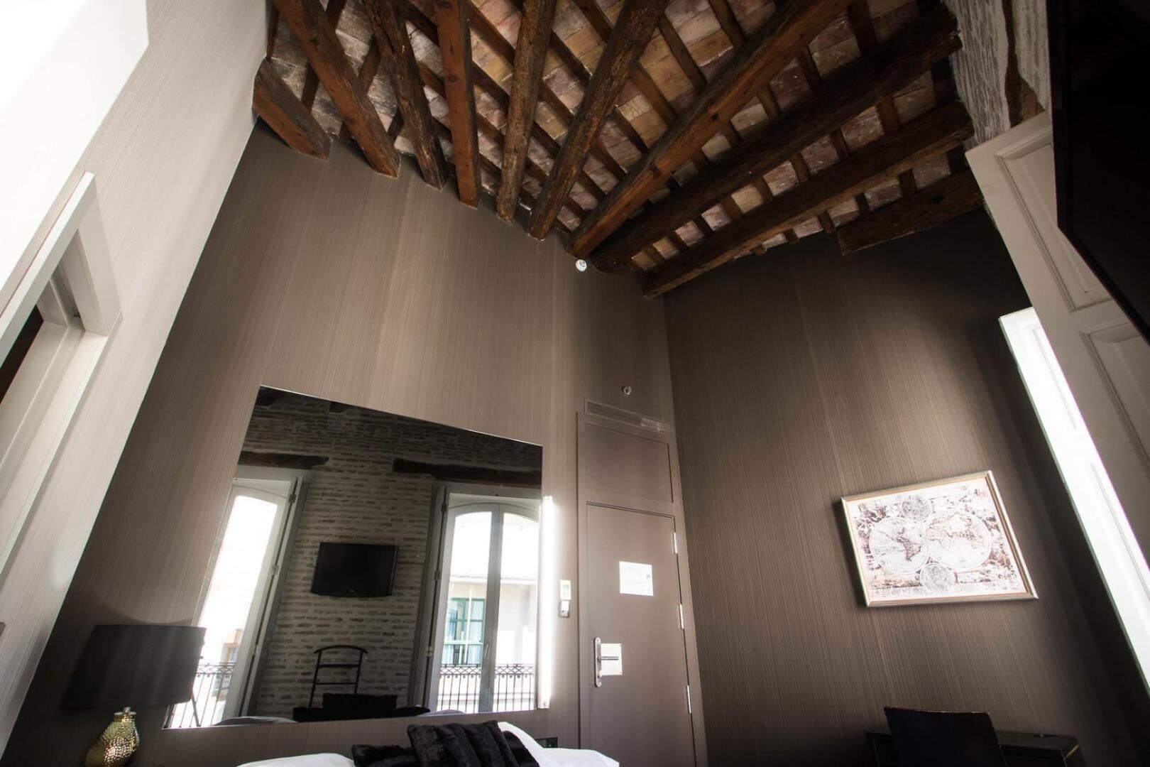 A room with a sloped ceiling, a brick wall, a large window, and a framed picture on the wall.