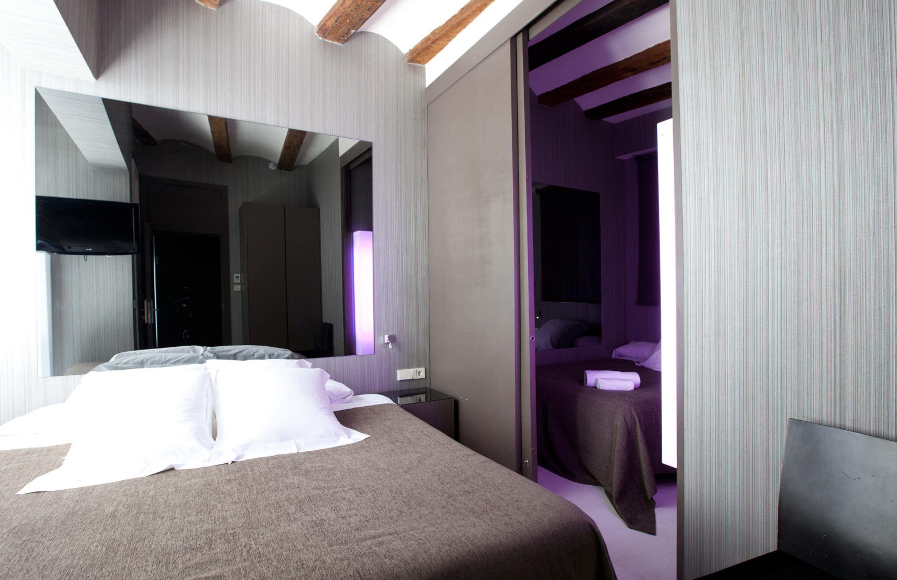 A modern hotel room with a large bed, a flat-screen TV, a mirror, and a bathroom with a bathtub and shower.
