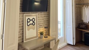 A room with a TV mounted on a brick wall, a framed picture on a table, a potted plant, and a coat rack with hanging clothes. - Cosy Rooms Embajador (Valencia)