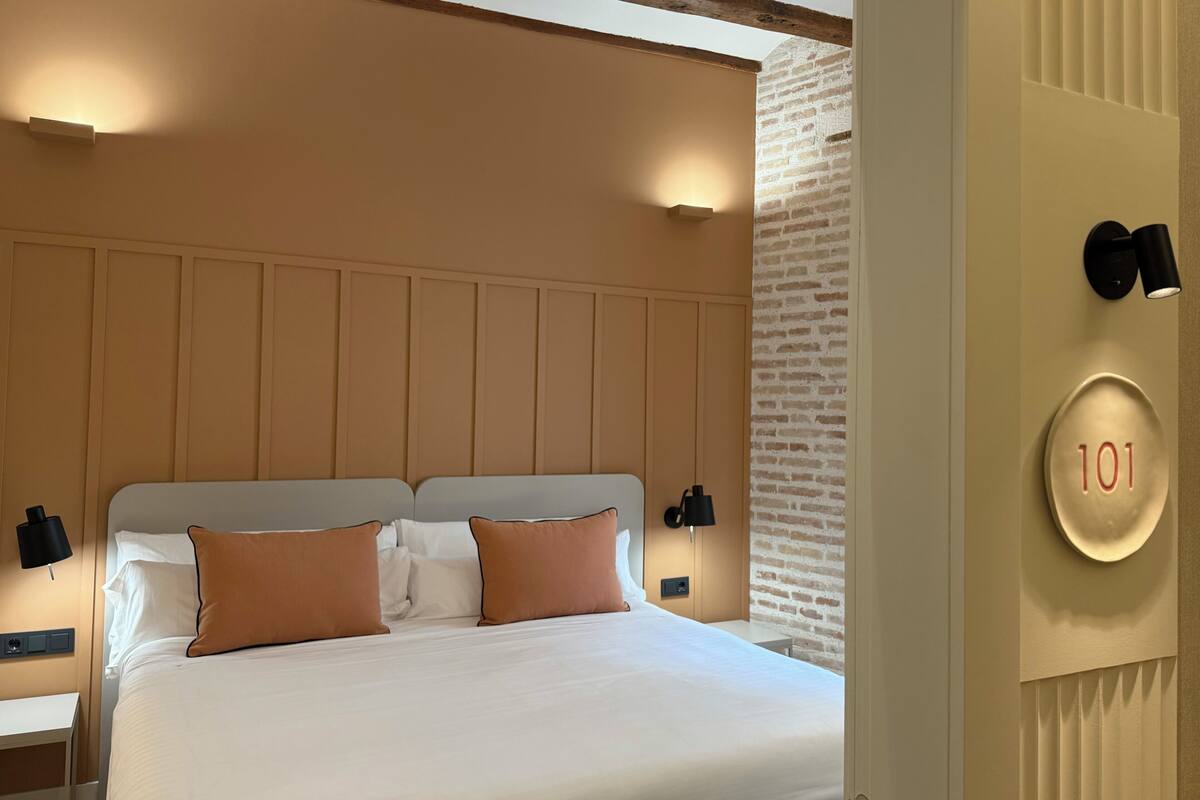 A hotel room with a large bed, two bedside tables, a wall-mounted light, and a number plate indicating room 101.