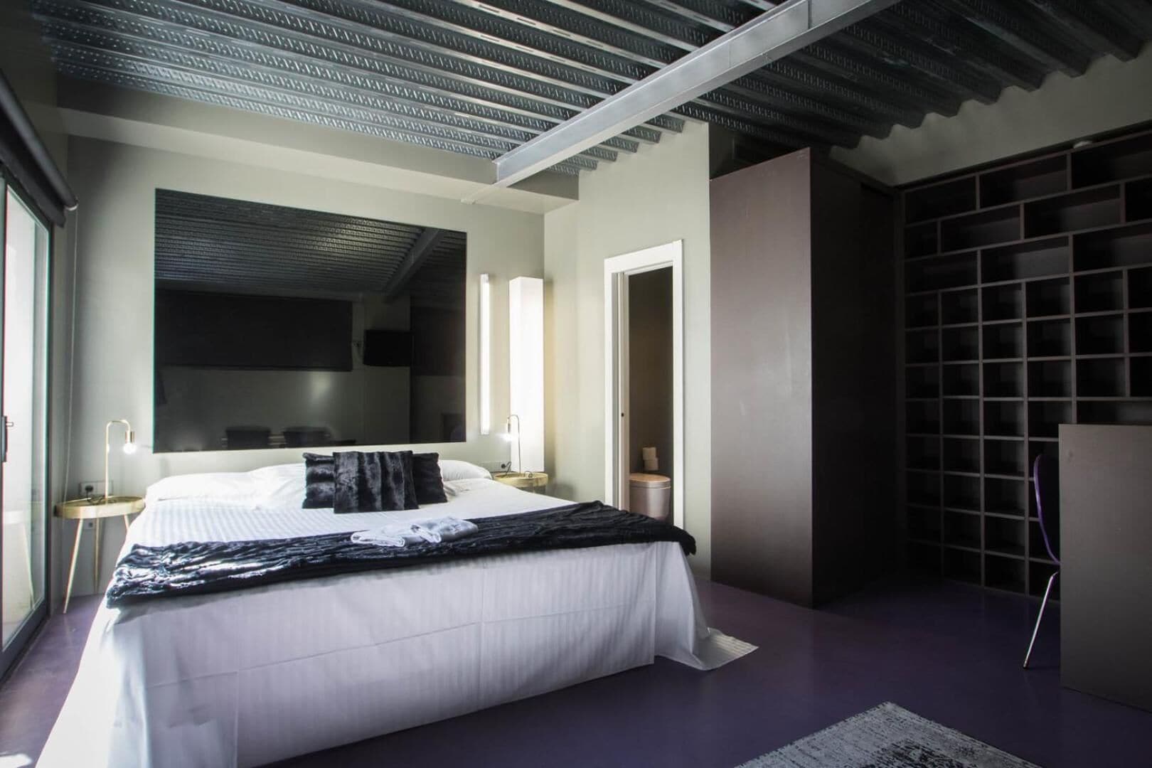 A modern bedroom with a large bed, a walk-in closet, and a view of the outdoors.