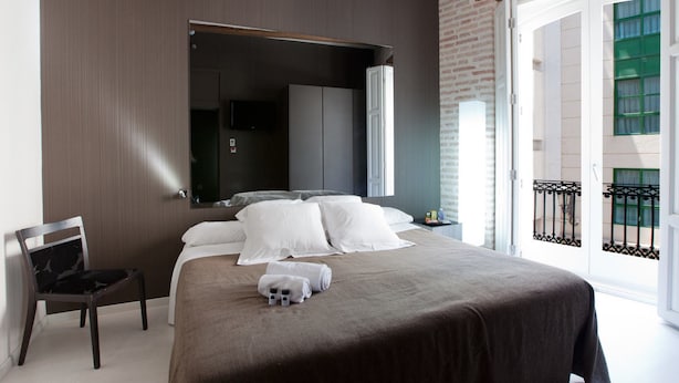 A modern hotel room with a large bed, a chair, a mirror, and a balcony with a view. - Cosy Rooms Embajador (Valencia)