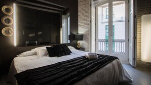 A hotel room with a large bed, a mirror, a TV, a balcony with a view, and a door. - Cosy Rooms Embajador (Valencia)