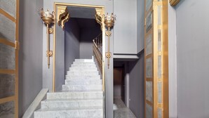 A marble staircase with golden railings and wall sconces, leading to a dark hallway. - Cosy Rooms Embajador (Valencia)