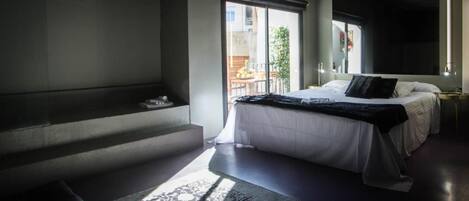 A modern bedroom with a large bed, a bench, and a view of the outside balcony.