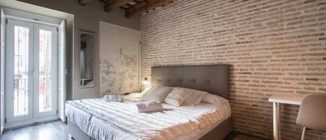 Un dormitorio con cama, una silla, un ventanal y una pared de ladrillo.