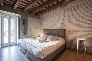 A bedroom with a bed, a chair, a window, and a brick wall. - Cosy Rooms Bolsería (Valencia)