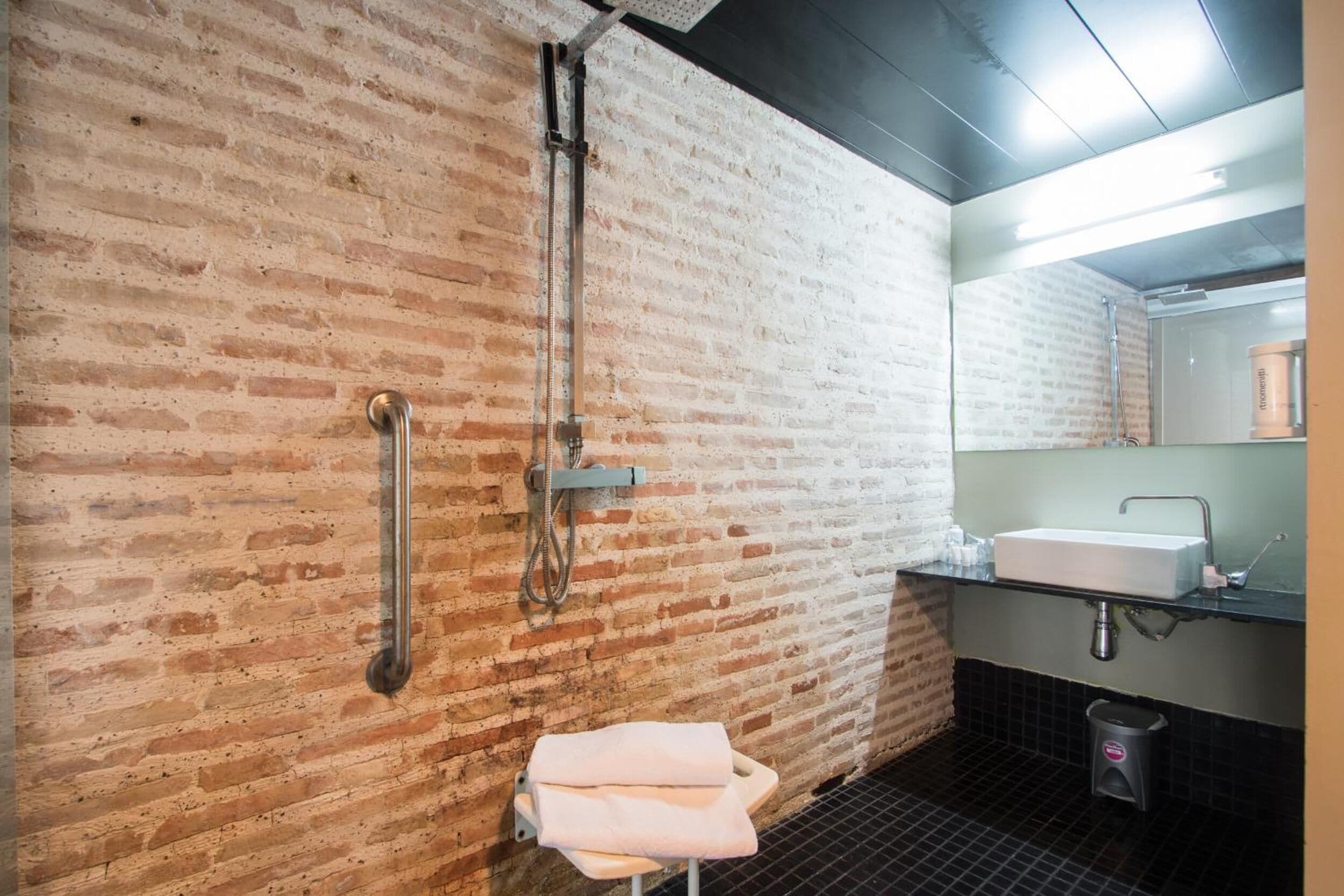 A bathroom with a brick wall, a shower, a sink, and a towel rack.