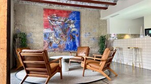 A modern lounge area with leather chairs, a round table, and a large abstract painting on the wall. - Cosy Rooms Bolsería (Valencia)