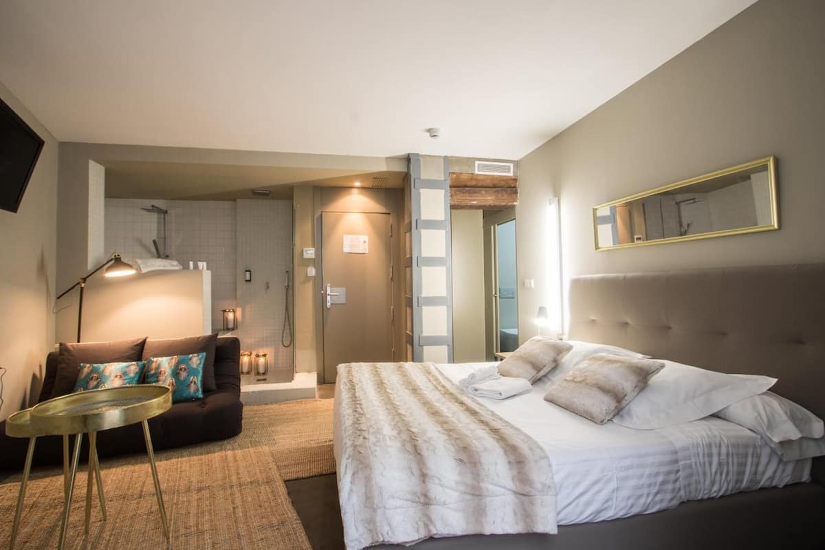 A modern hotel room with a large bed, a sofa, a small round table, and a mirror on the wall.
