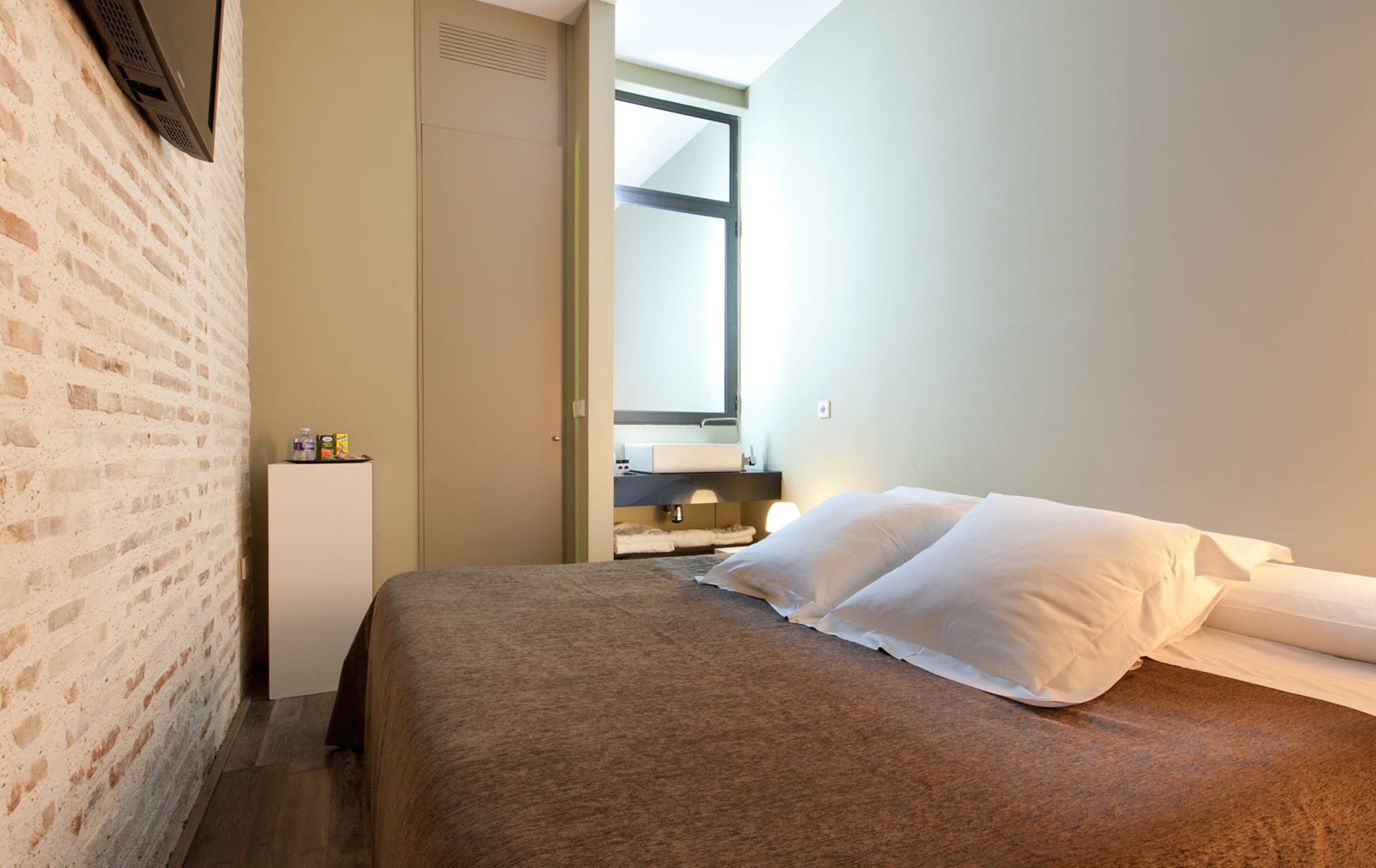 A hotel room with a bed, a small bedside table, a mirror, and a window.