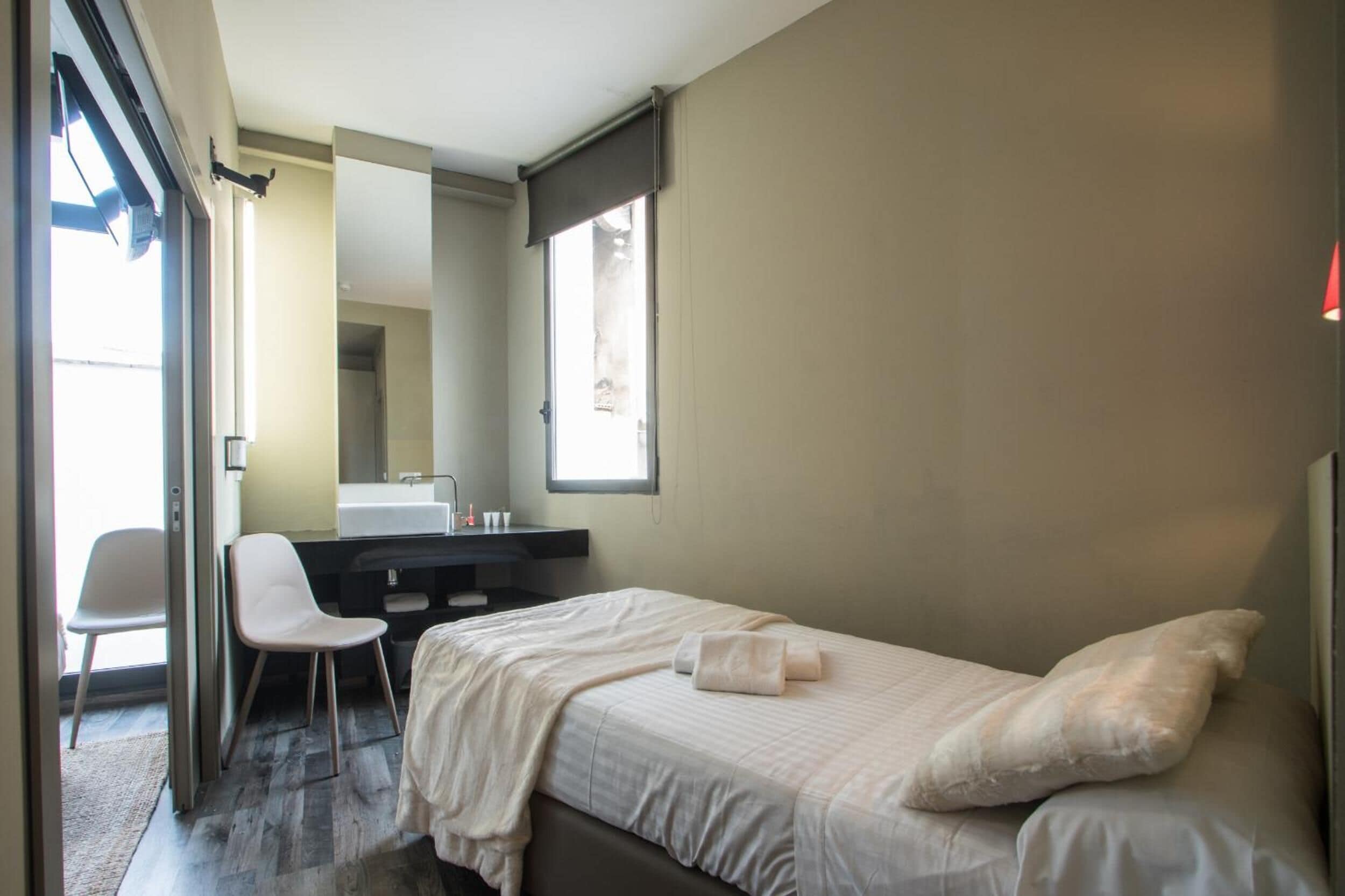 A bedroom with a bed, a chair, a desk, and a large mirror.