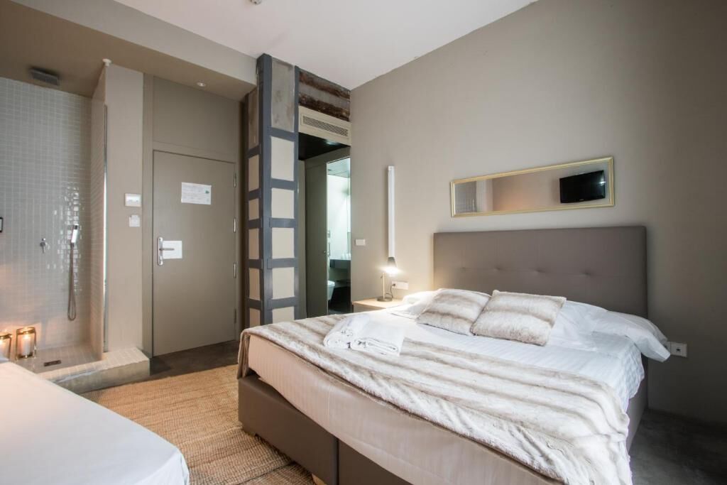 A modern hotel room with a large bed, a walk-in shower, and a small bedside table with a lamp.