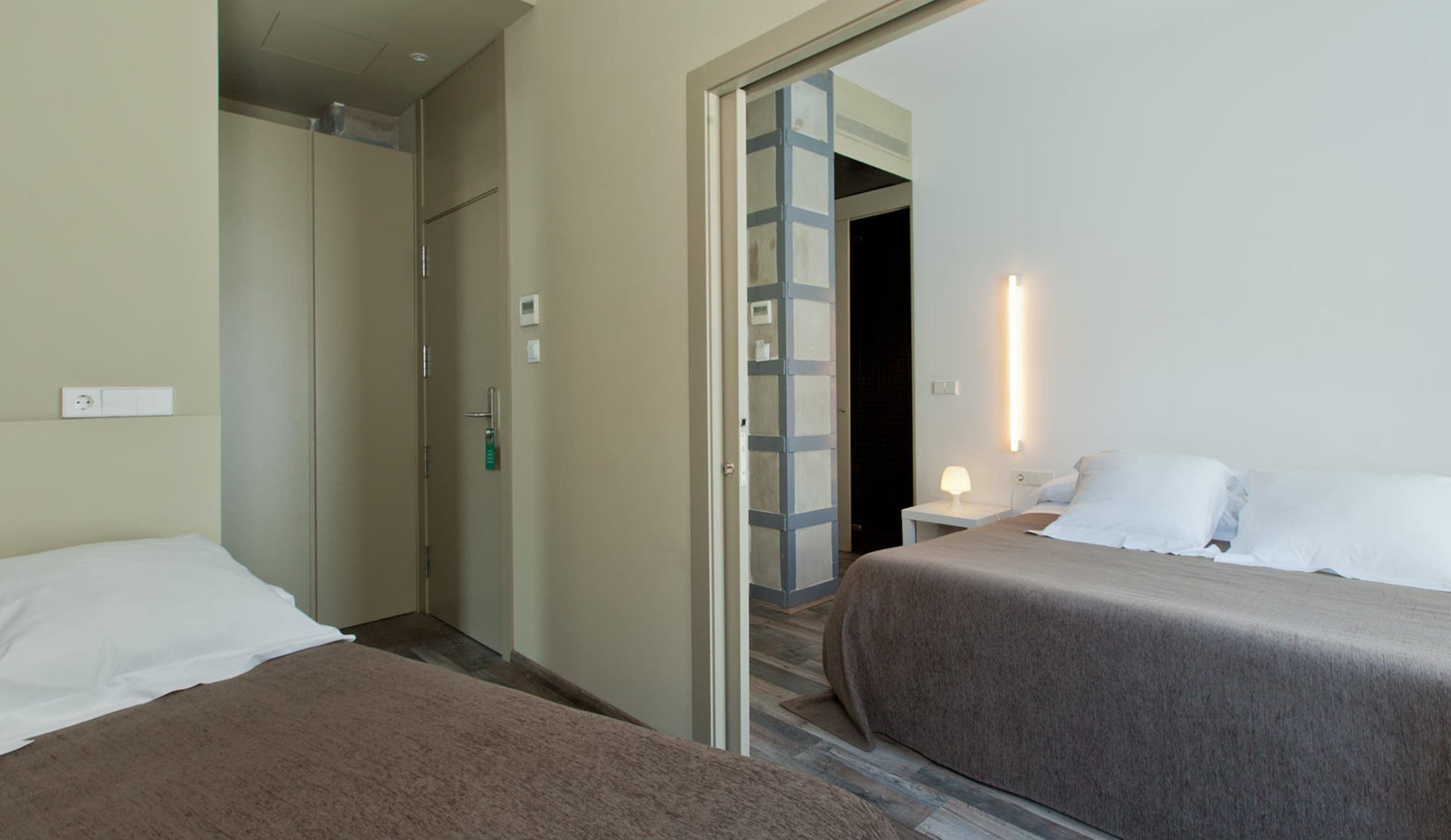 A hotel room with two beds, a bathroom, and a hallway leading to another room.