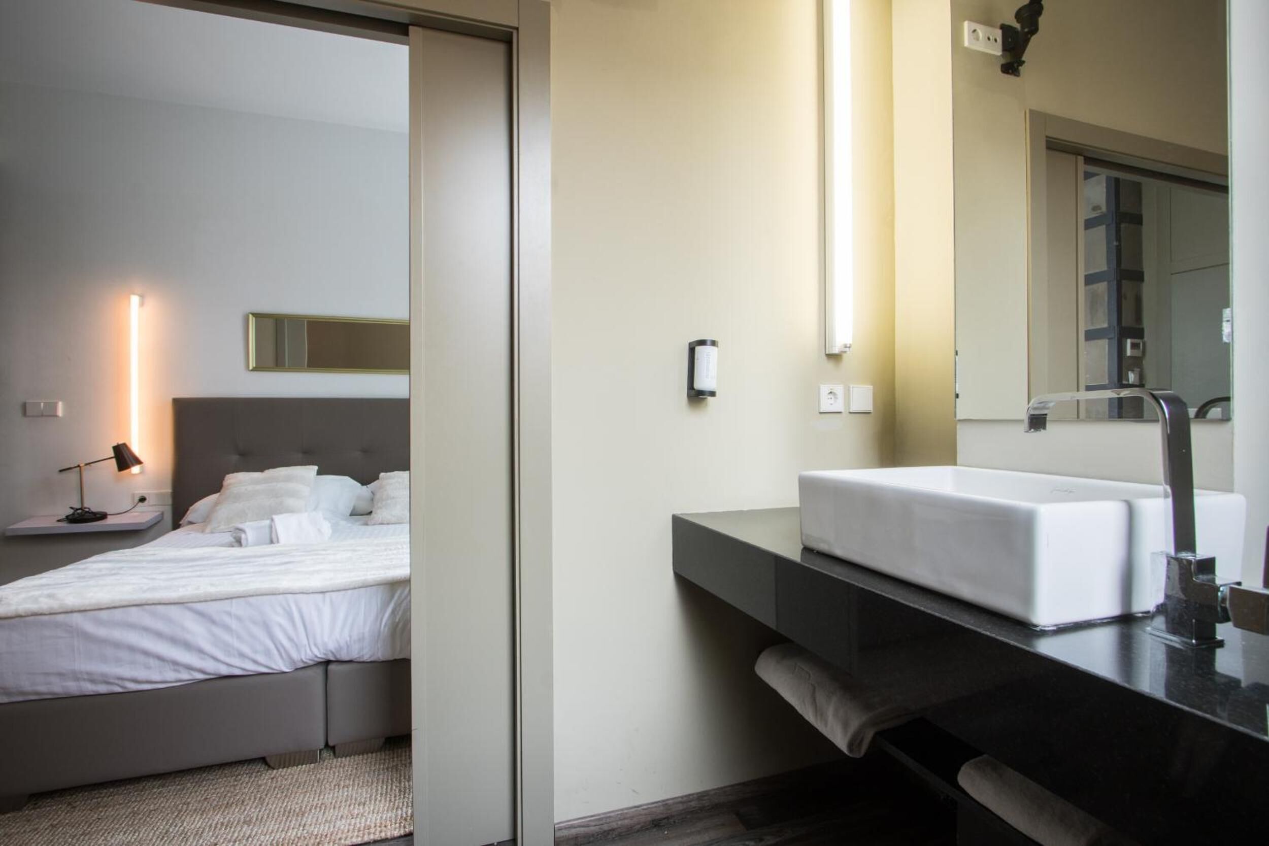 Et moderne hotelværelse med seng, sengetår og et badeværelse med vask og spejl.