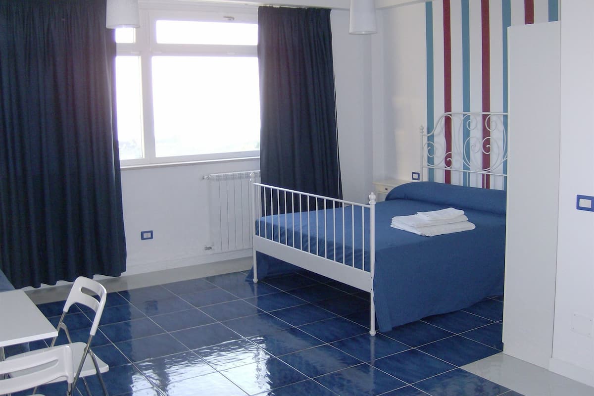A room with a single bed, a chair, a radiator, a window with curtains, and a striped wall.