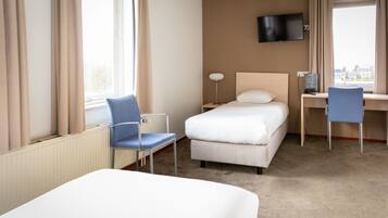 Une chambre d’hôtel comprenant un lit, un bureau avec une chaise, un téléviseur fixé au mur et une fenêtre avec des rideaux.