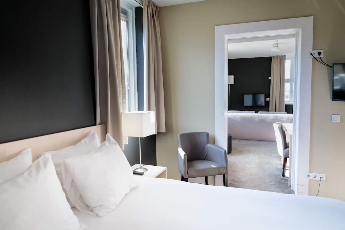 Habitación de hotel con cama, una silla, un escritorio con lámpara, televisión y vista al comedor.