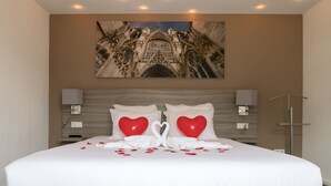 Ein Hotelzimmer mit einem großen Bett, einem Kopfteil mit einer Zierleiste, einem Wandbild einer Kathedrale und einem Nachttisch mit einer Lampe.