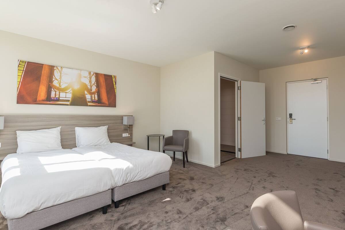 Habitación de hotel con una cama grande, una mesita, una silla y una puerta.