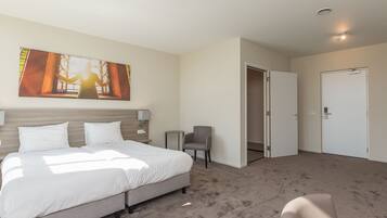 Habitación de hotel con una cama grande, una mesita, una silla y una puerta.