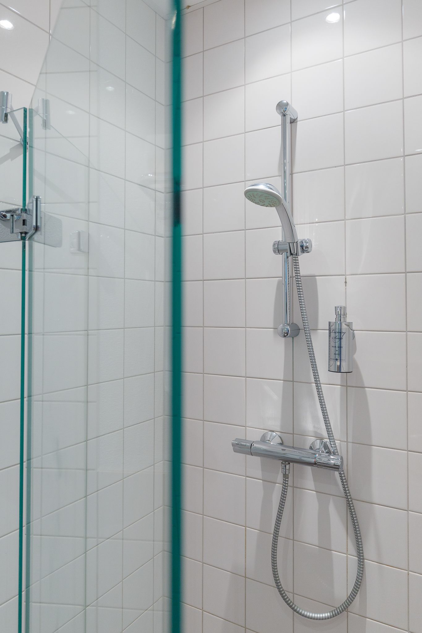 A modern shower with a handheld showerhead and a fixed showerhead, mounted on a tiled wall.