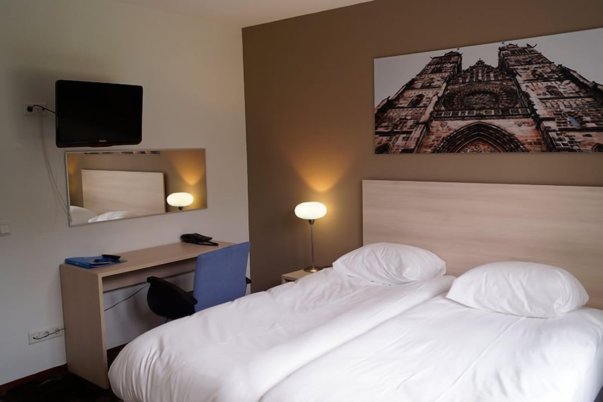 Een hotelkamer met een bed, een bureau met stoel, een bureaulamp, een telefoon en een televisie aan de muur.