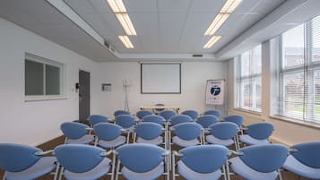 Une salle de conférence avec des rangées de chaises bleues, un écran de projection et un tableau blanc.