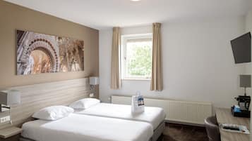 Een hotelkamer met twee bedden, een groot raam met gordijnen, een flatscreen televisie, een bureau met een lamp en een radiator.
