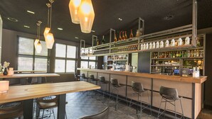 Eine Bar mit einer Holztheke, mehreren Hockern sowie einer Auswahl an Flaschen und Gläsern auf Regalen.