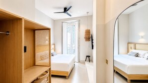 Un dormitorio moderno con dos camas, un ventilador de techo, una cesta de mimbre y un espejo grande.