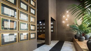 Un vestíbulo con documentos enmarcados en la pared, suelo de baldosas blanco y negro, y una planta a la derecha.