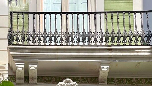 Un balcón con barandillas de hierro forjado decorativas y un arco ornamentado.