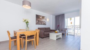 Una sala de estar moderna con una mesa de comedor, un sofá y sillas. Hay un cuadro en la pared y una ventana con cortinas.