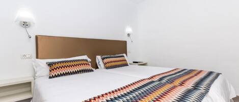 A hotel room with a large bed, two pillows, a nightstand, and a wall-mounted lamp.