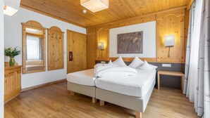 A wooden-paneled bedroom with two beds, a mirror, wall sconces, and a bench. - Hotel Burgstall (Neustift Im Stubaital)