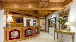 A reception area with a wooden reception desk, a mirror, and framed artwork on the walls. - Hotel Burgstall (Neustift Im Stubaital)