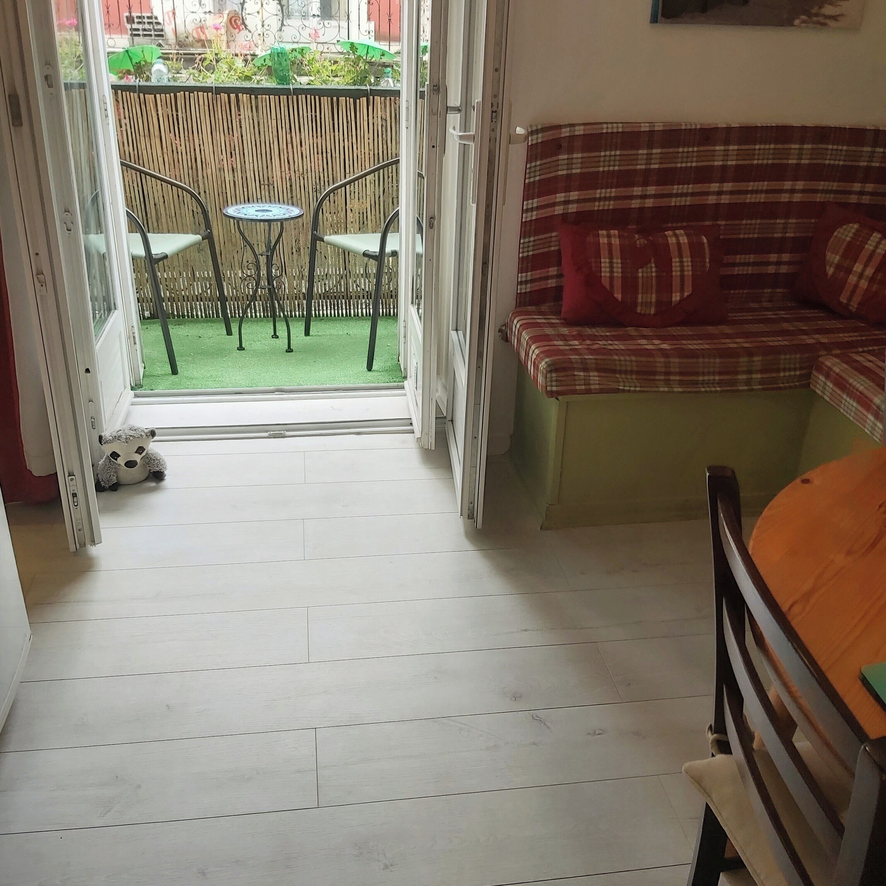 A room with a wooden floor, a sofa with plaid cushions, a small table, and a chair.
