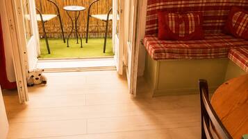 Een kamer met een houten vloer, een ruitjesbank met rode kussens, een klein rond tafeltje en twee stoelen.