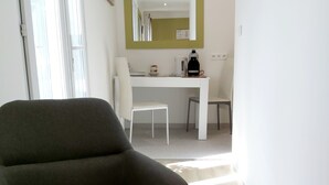 Une pièce moderne avec un fauteuil gris, un bureau blanc et un miroir au mur.