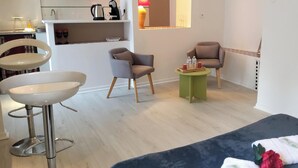 Une chambre d’hôtel moderne comprenant un lit, deux fauteuils, une petite table avec un plateau contenant divers objets, un lavabo et un miroir.
