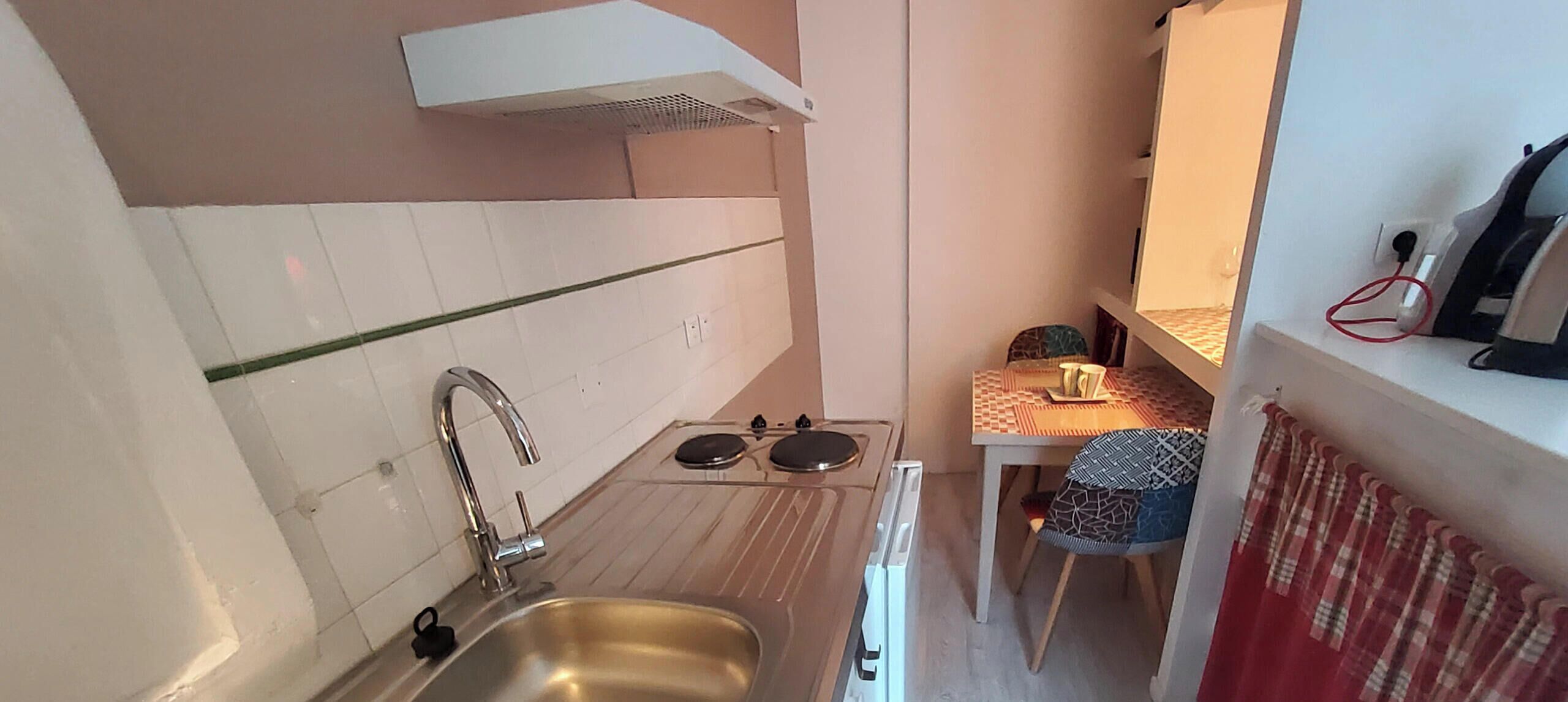 Une cuisine de taille réduite, équipée d’un évier, d’une cuisinière et de meubles blancs.