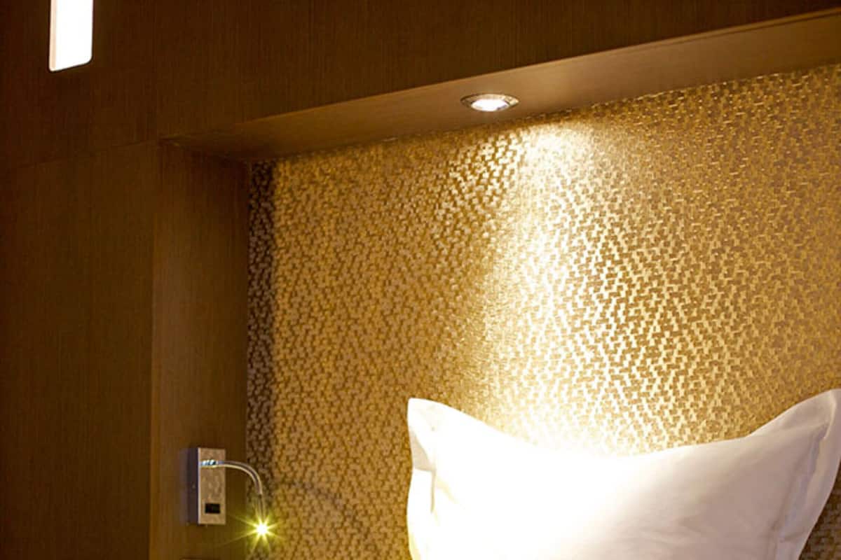 A hotel room with a bed, a nightstand, and a wall-mounted light fixture.